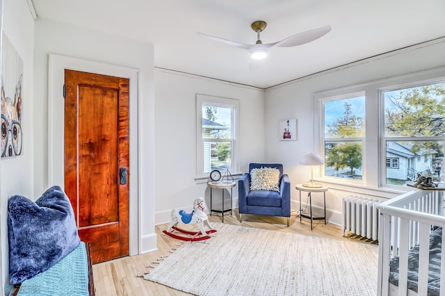 bedroom featuring a crib, ornamental molding, light wood-type flooring, radiator heating unit, and ceiling fan