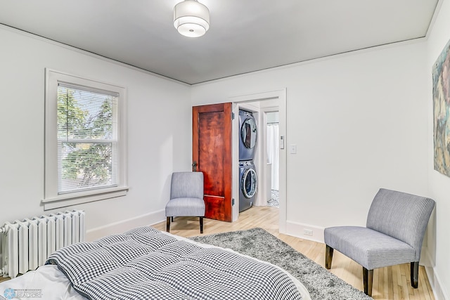 bedroom with stacked washer and clothes dryer, a closet, radiator, a walk in closet, and light hardwood / wood-style floors