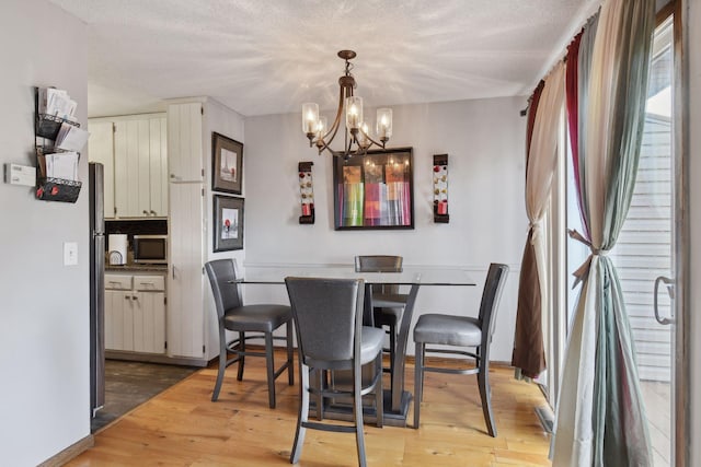 dining room with light hardwood / wood-style floors, a textured ceiling, and a chandelier