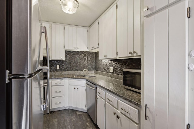 kitchen featuring white cabinetry, sink, dark wood-type flooring, dark stone countertops, and appliances with stainless steel finishes