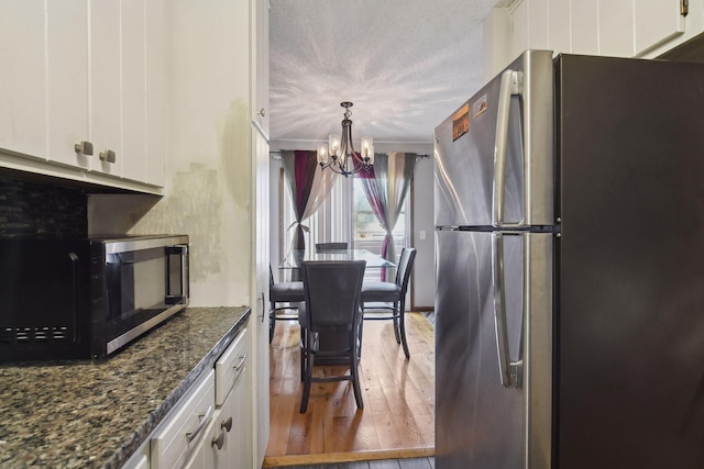 kitchen with stainless steel appliances, an inviting chandelier, light hardwood / wood-style flooring, dark stone countertops, and white cabinets