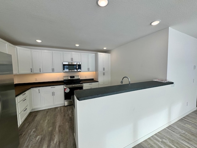 kitchen featuring hardwood / wood-style flooring, kitchen peninsula, appliances with stainless steel finishes, a textured ceiling, and white cabinets