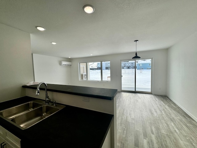 kitchen with decorative light fixtures, a wall mounted AC, sink, light wood-type flooring, and a textured ceiling