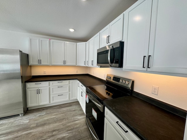 kitchen with light hardwood / wood-style floors, white cabinetry, stainless steel appliances, and a textured ceiling