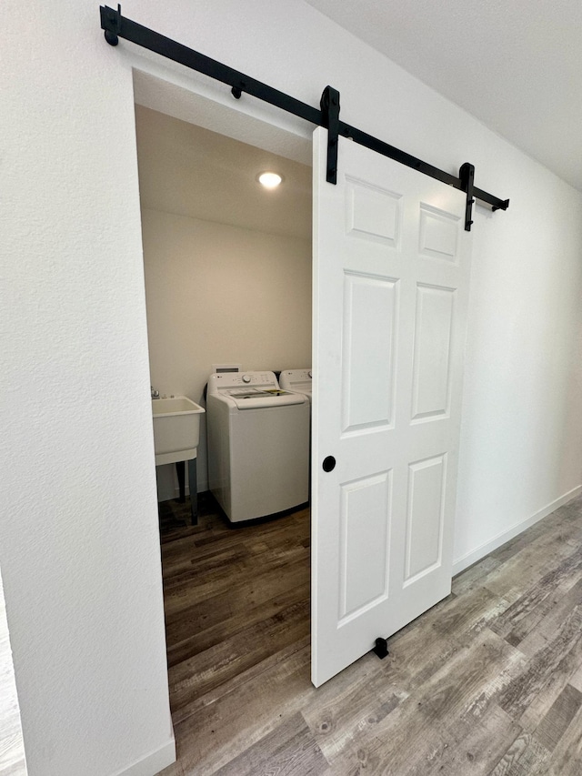 clothes washing area featuring separate washer and dryer, a barn door, hardwood / wood-style flooring, and sink