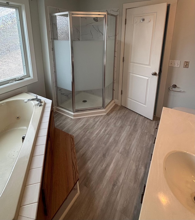 full bathroom with a jetted tub, wood finished floors, a sink, and a stall shower