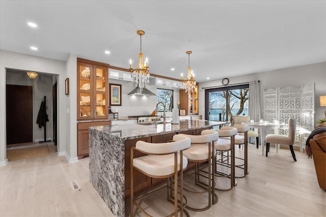 bar with an inviting chandelier, pendant lighting, light hardwood / wood-style floors, and light stone countertops