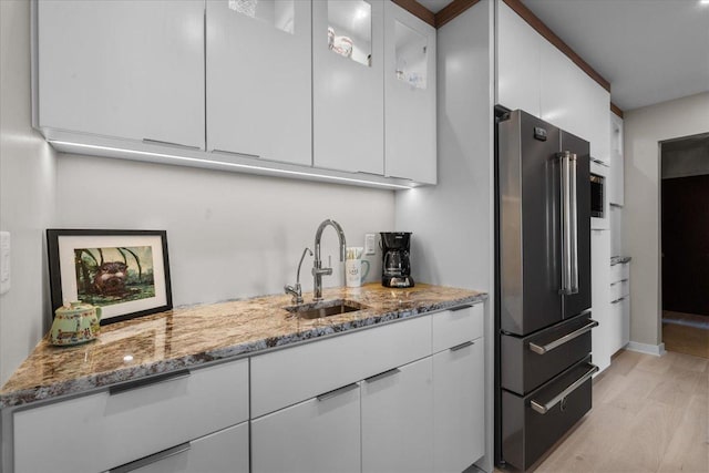 kitchen with sink, white cabinets, light stone counters, and high end fridge