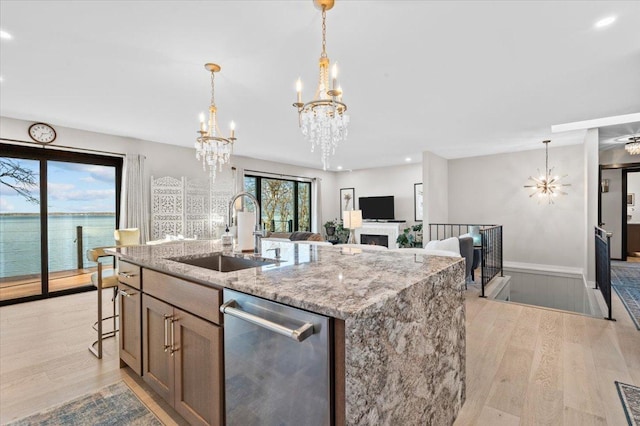 kitchen with a kitchen island with sink, light wood-type flooring, dishwasher, a water view, and sink