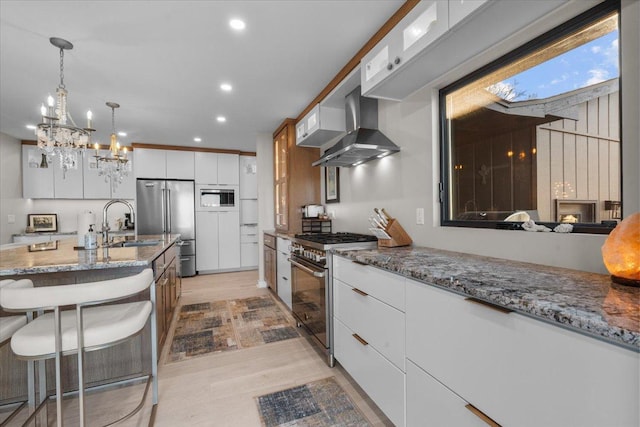 kitchen featuring wall chimney exhaust hood, white cabinetry, high end appliances, a breakfast bar, and light hardwood / wood-style flooring