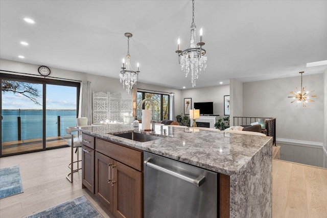 kitchen with sink, a water view, light wood-type flooring, stainless steel dishwasher, and a center island with sink