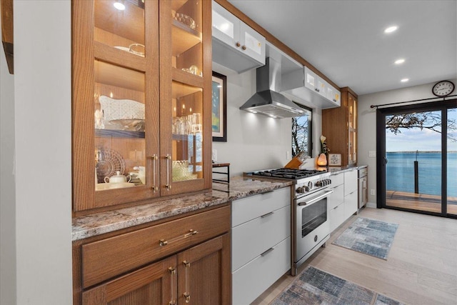 kitchen with high end stainless steel range oven, light stone counters, white cabinets, and a water view