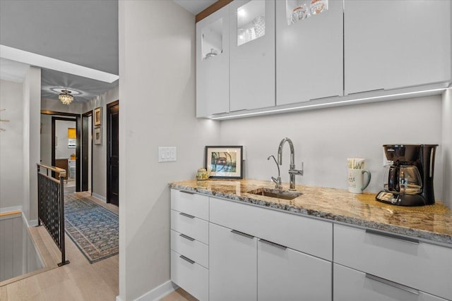 bar featuring light stone countertops, white cabinets, and sink