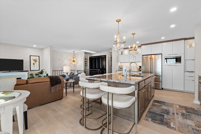 kitchen featuring sink, light wood-type flooring, a kitchen island with sink, appliances with stainless steel finishes, and white cabinets