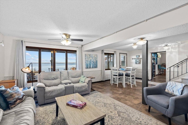 living room with ceiling fan, a textured ceiling, wood-type flooring, and a water view