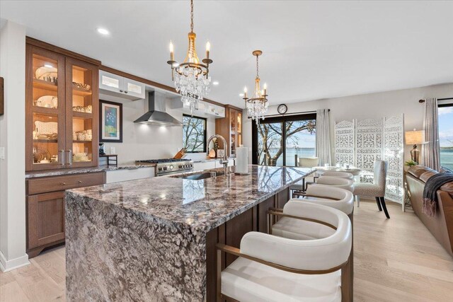kitchen featuring high end stainless steel range, a sink, light wood-type flooring, wall chimney exhaust hood, and a notable chandelier