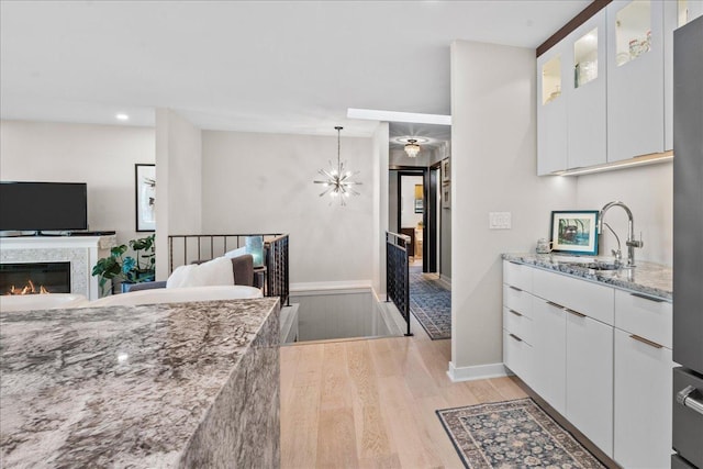 kitchen with white cabinets, a sink, baseboards, light wood-style floors, and light stone counters