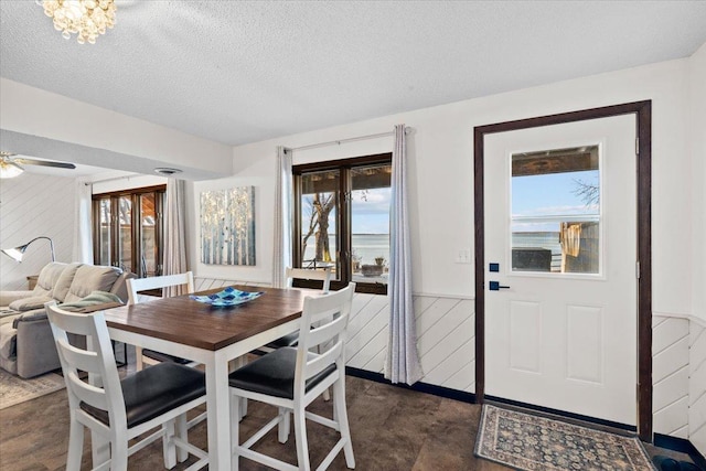 dining area featuring wooden walls, a textured ceiling, a wainscoted wall, and ceiling fan