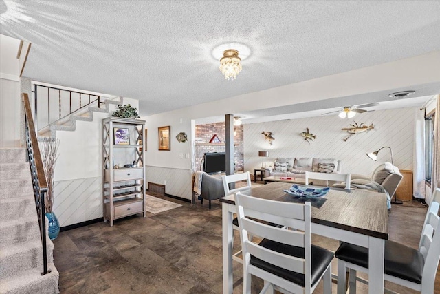 dining area featuring stairs, ceiling fan, a wainscoted wall, wood walls, and visible vents