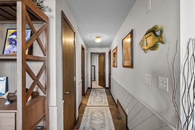 hall with a decorative wall, a textured ceiling, and a wainscoted wall