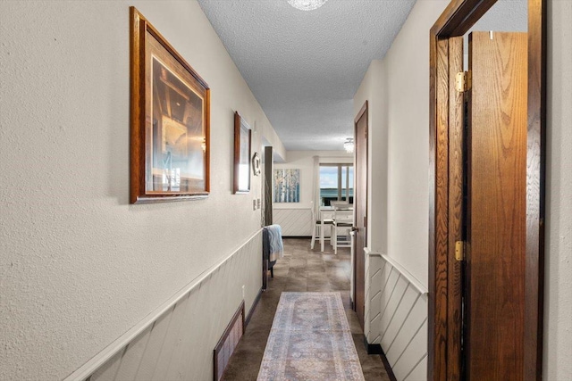 corridor featuring a textured ceiling, a textured wall, visible vents, and wainscoting
