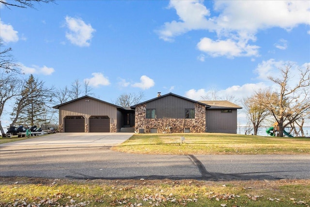 ranch-style house featuring driveway, stone siding, a front yard, and a garage