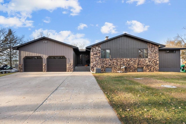 ranch-style home featuring concrete driveway, stone siding, a front yard, and a garage