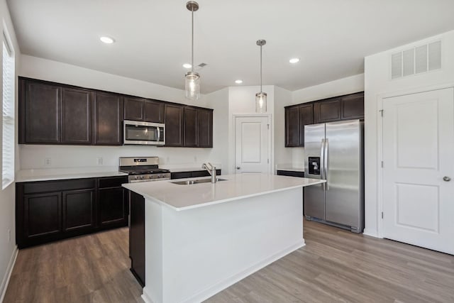 kitchen with hardwood / wood-style flooring, a center island with sink, sink, decorative light fixtures, and appliances with stainless steel finishes