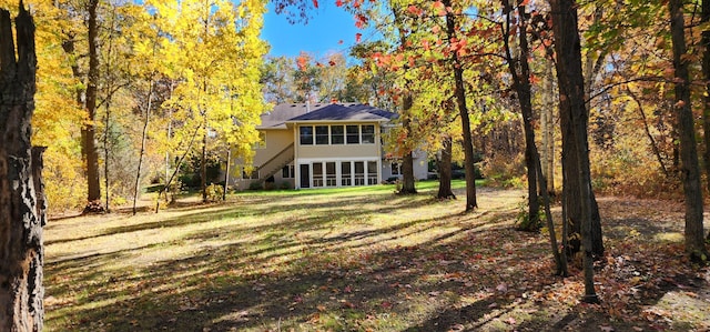 view of front facade featuring stairway, a view of trees, a front lawn, and a sunroom