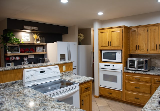 kitchen with white appliances, light stone counters, light tile patterned floors, brown cabinetry, and backsplash