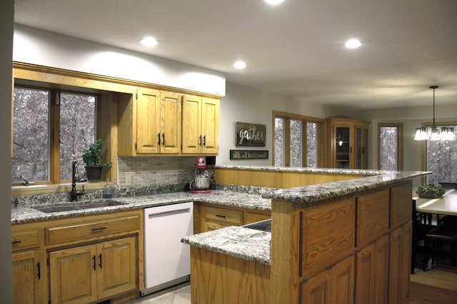 kitchen with a sink, backsplash, a peninsula, white dishwasher, and stone counters