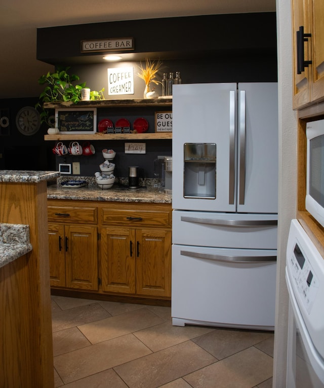 kitchen featuring tile patterned floors, washer / clothes dryer, white fridge with ice dispenser, and brown cabinets