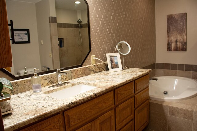 full bath with tiled shower, a tub with jets, and vanity