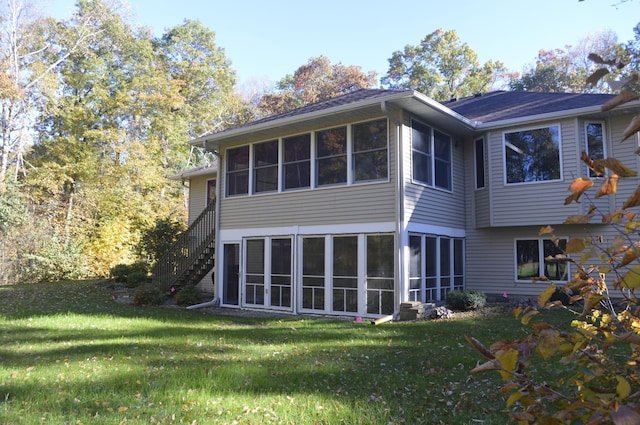 rear view of property featuring stairs, a lawn, and a sunroom