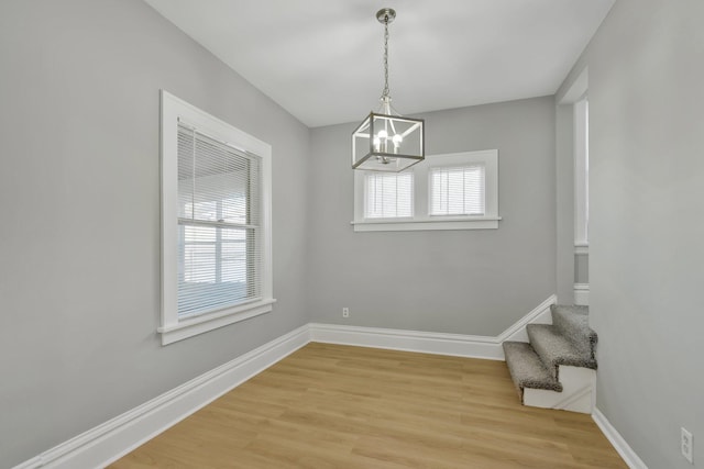 unfurnished dining area with an inviting chandelier and light wood-type flooring