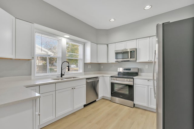 kitchen with appliances with stainless steel finishes, light hardwood / wood-style flooring, white cabinets, and sink