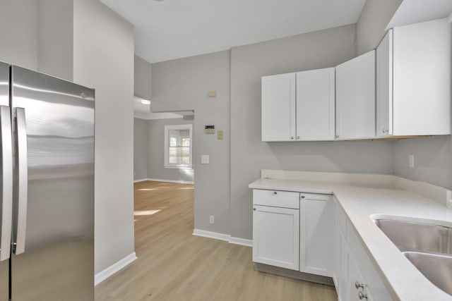 kitchen with light hardwood / wood-style floors, stainless steel refrigerator, sink, and white cabinets