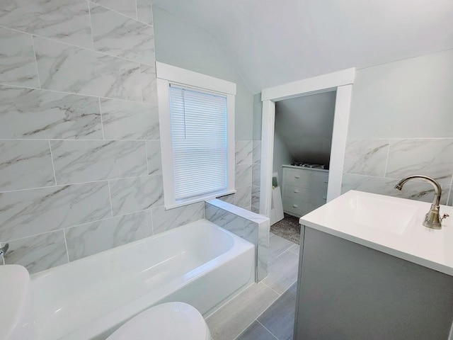 bathroom with tile walls, vaulted ceiling, toilet, a washtub, and vanity