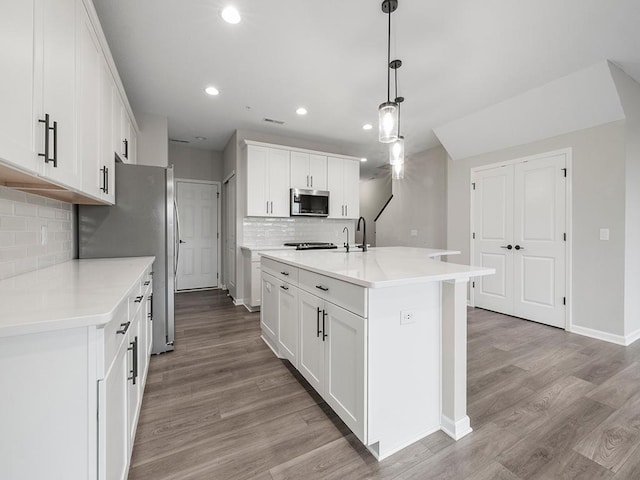 kitchen with white cabinetry, stainless steel appliances, an island with sink, pendant lighting, and light wood-type flooring