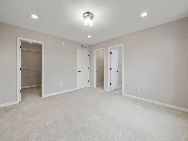 unfurnished bedroom featuring ensuite bath, light colored carpet, a spacious closet, and a closet