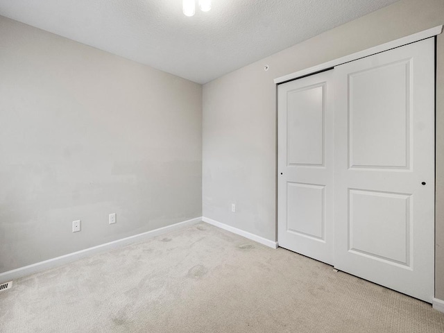 unfurnished bedroom featuring a closet, light colored carpet, and a textured ceiling