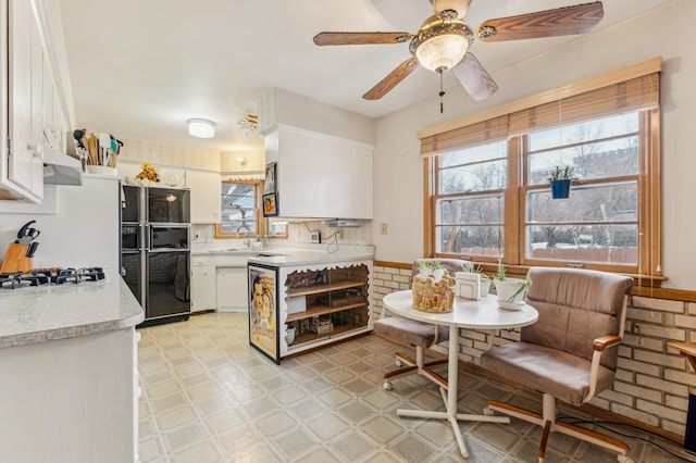 kitchen featuring range hood, sink, white cabinets, black fridge, and white gas cooktop