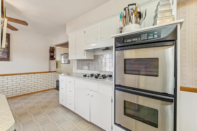 kitchen with brick wall, double oven, white cabinetry, ceiling fan, and white gas cooktop