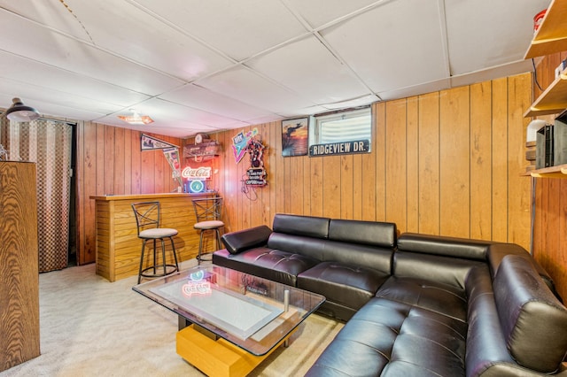 living room with bar, light carpet, a paneled ceiling, and wood walls