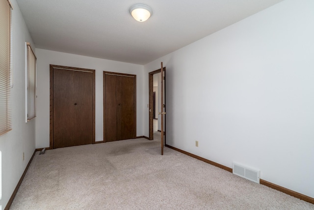 unfurnished bedroom with light colored carpet and two closets