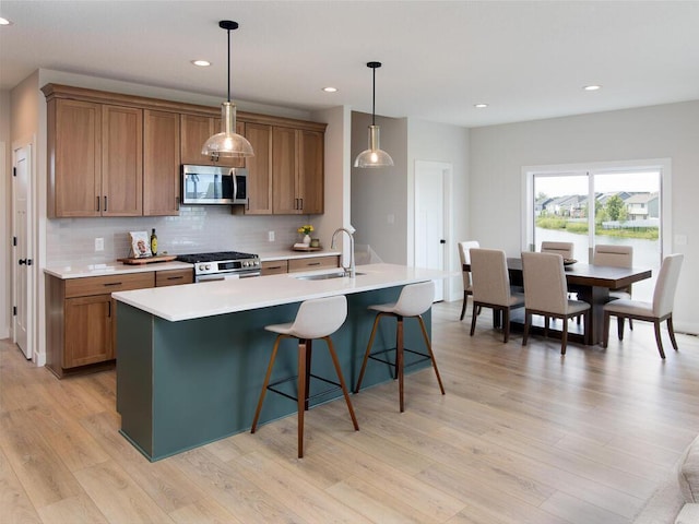kitchen featuring decorative backsplash, brown cabinetry, appliances with stainless steel finishes, a sink, and light wood-type flooring