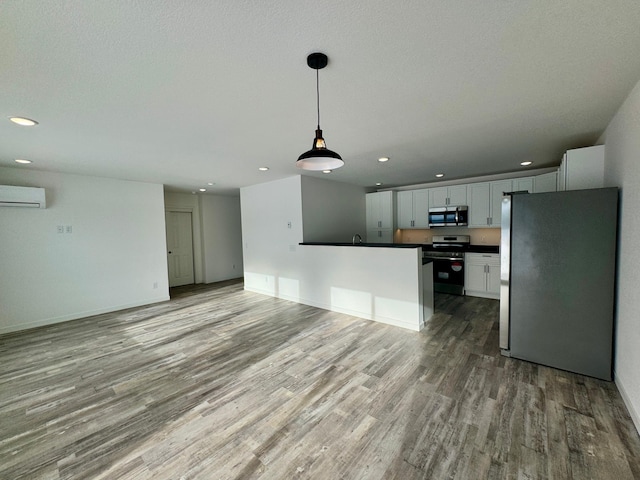 kitchen with white cabinetry, stainless steel appliances, light wood-type flooring, pendant lighting, and an AC wall unit