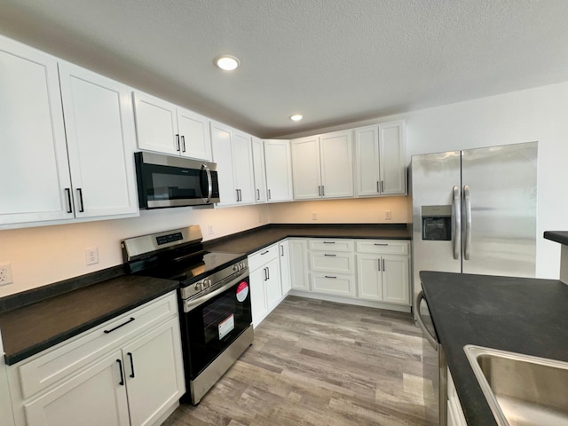 kitchen with white cabinetry, light hardwood / wood-style flooring, stainless steel appliances, and a textured ceiling