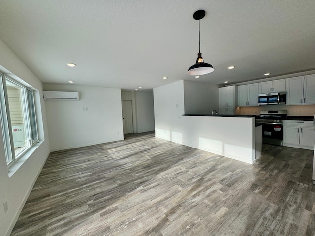 kitchen featuring an AC wall unit, white cabinetry, stainless steel appliances, hanging light fixtures, and hardwood / wood-style flooring