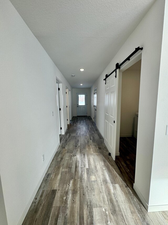 hall featuring a barn door, wood-type flooring, and a textured ceiling